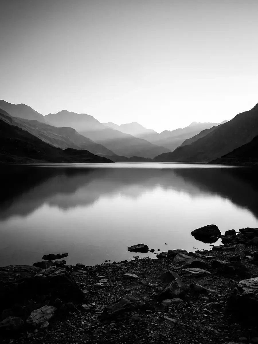 An alpine lake at dawn with layered ridges, black and white