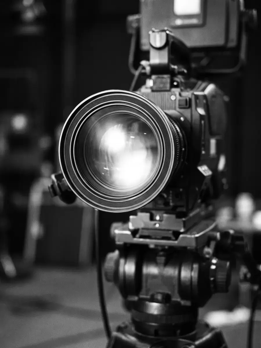 A broadcast camera lens on a tripod head, black and white